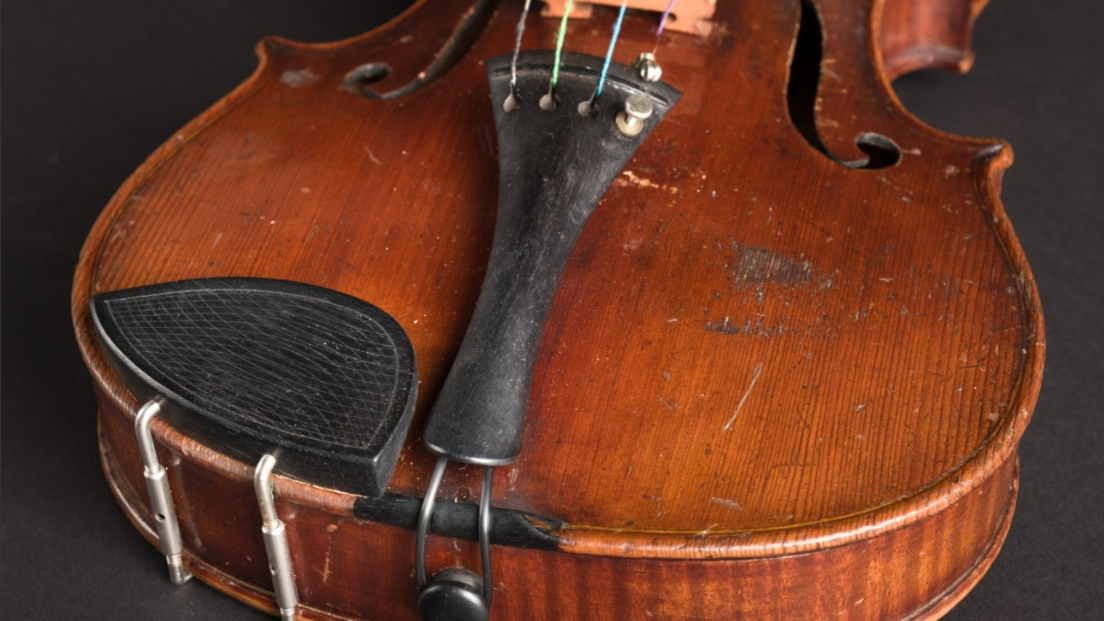 A close-up of the violin shows a slightly worn wooden frame and four strings.